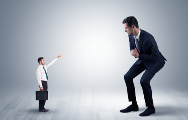 Small businessman in shirt pointing to an afraid businessman
