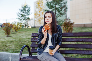 Handsome caucasian woman sitting in park and eating croissant