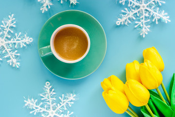 Cup of coffee with artificial yellow tulips and snowflake ornaments on blue background for drinks and beverage in winter season concept