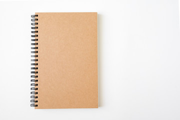 Top view of closed spiral blank craft paper cover notebook with pencil on white desk background