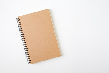 Top view of closed spiral blank craft paper cover notebook with pencil on white desk background