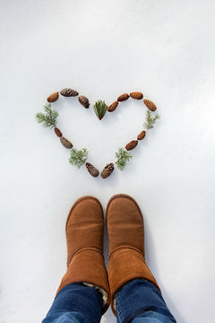 Feet In snow over a heart made of pinecones and pine