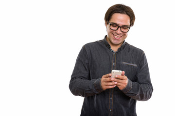 Studio shot of young happy Persian man smiling while using mobil