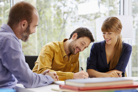 Woman And Advisor Looking At Man Signing Paper