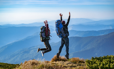The man and a woman with backpacks jumping on the mountain