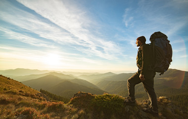 The man standing with a camping backpack on the rock with a picturesque sunrise