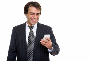 Studio shot of young happy Persian businessman smiling while usi