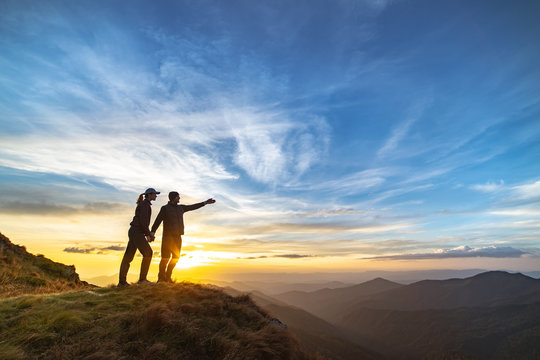 The Couple Gesturing On The Mountain With A Picturesque Sunset