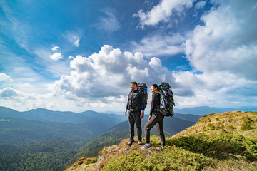 The young couple on the mountain on the picturesque cloudscape background