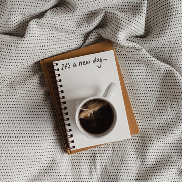 A journal with words ""It's a new day..."" handwritten on a page with a mug of tea