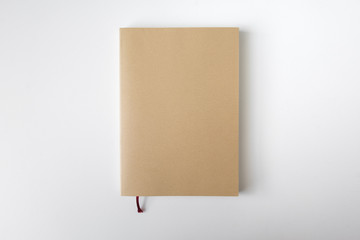Top view of closed blank craft paper cover notebook with pencil on white desk background - obrazy, fototapety, plakaty