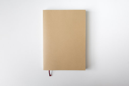 Top view of closed blank craft paper cover notebook with pencil on white desk background
