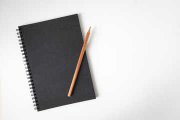 Top view of notebook black cover with wood texture pencil on white desk background