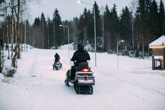 back view shot of two unrecognizable people riding snowmobiles