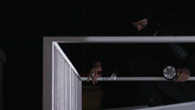Caucasian man with scrap and flashlight in hands trying to commit crime. Masked man in black clothes in balcony. Lifestyle.