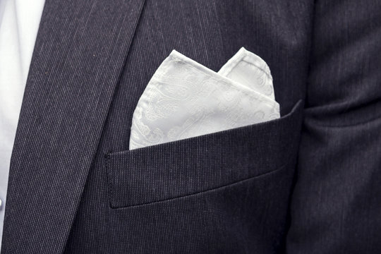 View to the male coat pocket with a fixed white square. Men's suit accessories. Wedding male guest's attire. Male wedding style. Formal dinner outfit for men. Elements of suit. Pocket square folding.