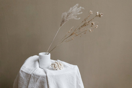 dried flower sprigs in white vase on linen table cloth