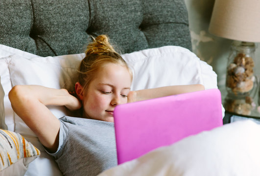 Preteen girl streaming a tv programme on her laptop in bed