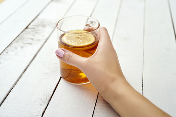 woman's hand with a glass of delicious hot tea with lemon on an old white wooden table