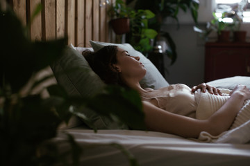 Side view of a young woman sleeping on bed at home.