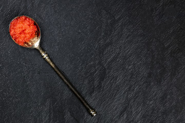 Fototapeta na wymiar Red fish roe in a spoon, shot from above on a black background with copy space