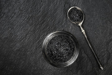 Black fish roe in a jar and in a spoon, shot from the top on a black background with a place for text