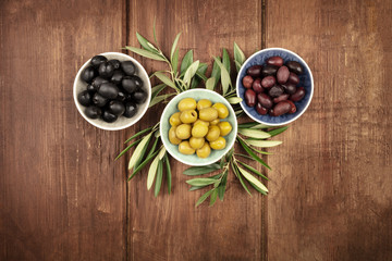 Obraz na płótnie Canvas Various olives in bowls with leaves, shot from the top on a dark wooden background with a place for text