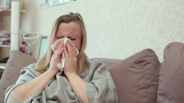 The woman blows her nose in a paper handkerchief. She has a cold, headache