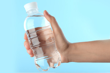 Woman holding plastic bottle with water on color background