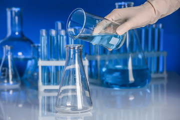 Scientist pouring liquid into flask on table. Laboratory analysis