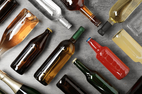 Bottles with different alcoholic drinks on grey background, flat lay