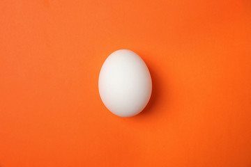 Raw chicken egg on color background, top view