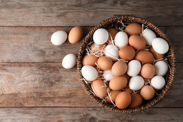 Basket with raw chicken eggs on wooden background, top view. Space for text