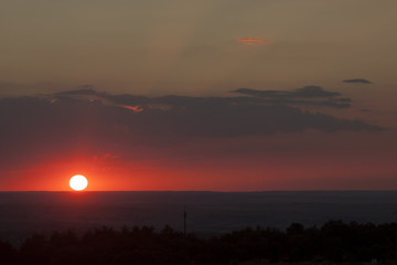Fototapeta premium Natural sun exposure on field or meadow. Bright dramatic sky and dark earth. Countryside landscape under scenic colorful sky at sunset. Sun over the horizon. Warm colors