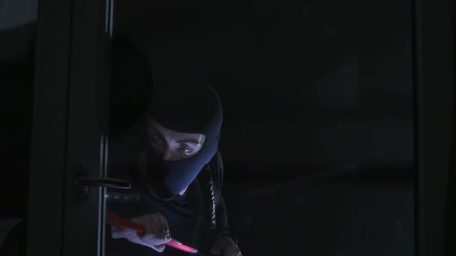 Tricky Caucasian thief in black balaclava picking lock with red scrap and getting easily into flat. Danger. Darkness. Night.