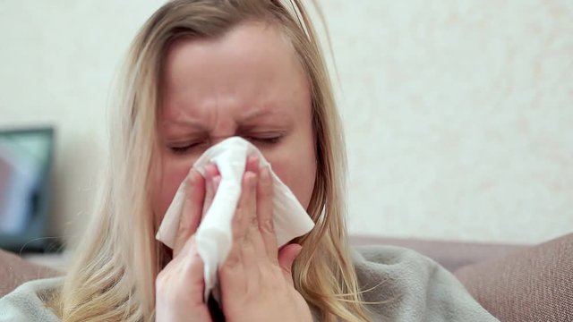 The woman blows her nose in a paper handkerchief. She has a cold, headache