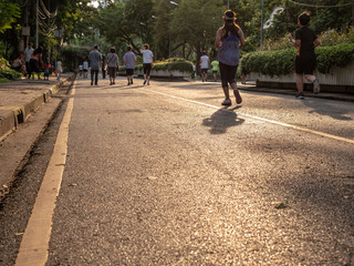 Selective focused on foreground at pathway with emotion blurred background. Rear view of people who are walking and running in public park. Low selection view of the way forward.