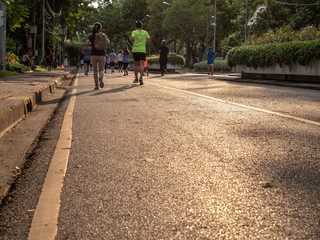 Selective focused on foreground at pathway with emotion blurred background. Rear view of people who are walking and running in public park. Low selection view of the way forward.