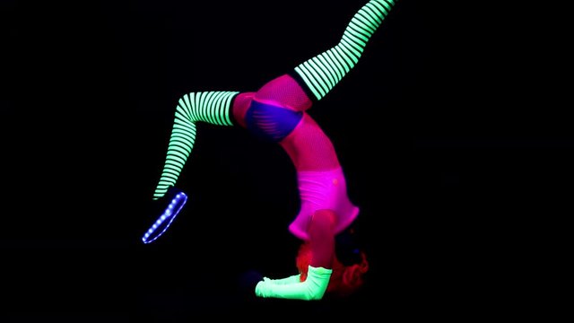amazing female yoga instructor moving between poses wearing fluorescent clothing under UV black light. the movement has been made to look like a fast back and forth loop