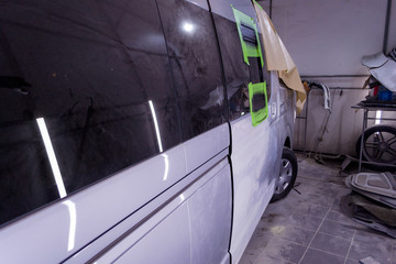Fototapeta premium Preparing for painting a silver bus in a body repair shop in a separate box service station. Putting putty and leveling the surface of the door before painting.