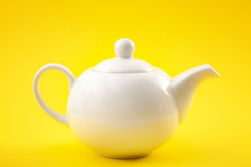 White ceramic teapot, china pot or tea kettle isolated on yellow background
