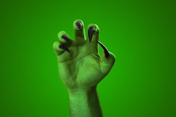 Halloween, nightmare creature and evil monster horror story concept with a scary zombie or demon hand with creepy long black nails isolated on green with a clip path cutout
