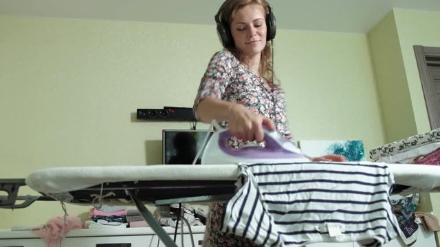 Woman Ironing The Mountain Of Laundry At Home In The Kitchen Listening To Music On Headphones And Dancing