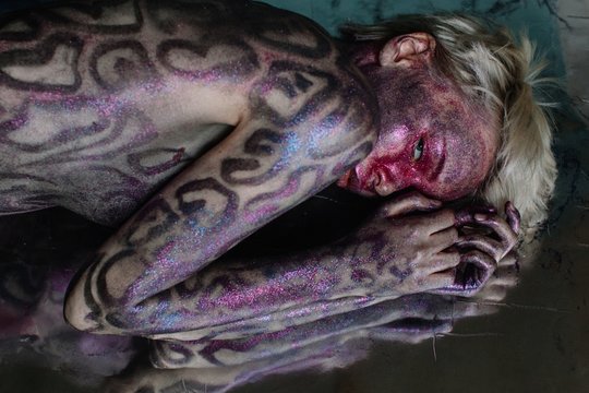 Young woman with shiny snake bodyart laying on reflecting floor