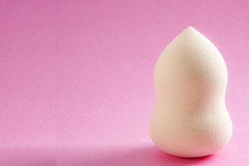 Face foundation application tool and makeup products concept with a beauty blender sponge isolated on a pink background and copy space