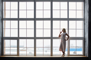 Fototapeta na wymiar Young blonde in light clothes, jacket, trousers and white shoes with a heel in the window