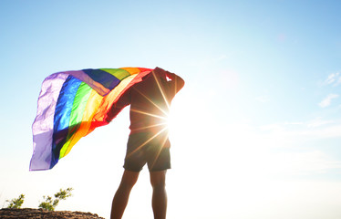 man standing on mountain top viewpoint raised rainbow LGBT flag to the sky