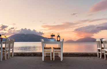 Fototapeta na wymiar Table served for two on seafront with bottle of wine, sign reserved, candle lighting and awesome sunset on background.