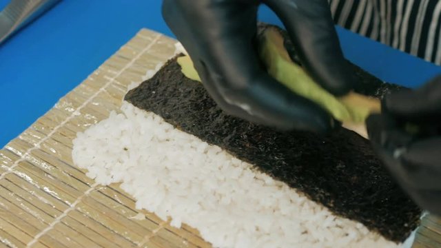Close-up of professional chef's hands in black gloves making sushi and rolls in a restaurant kitchen. Japanese traditional food. Preparation process. step by step