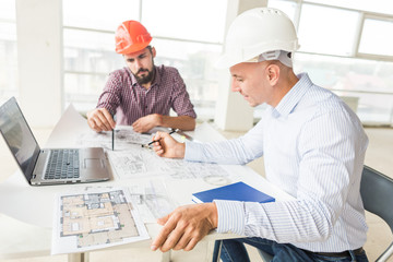 male engineers, architects working at the desk in helmets. Drawings, laptop, roulette on the desktop. Reception and supervision of building construction